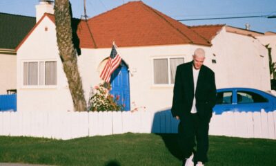 An adult standing outside a modest childhood house, looking back at it, late afternoon, quiet not sentimental