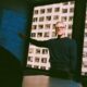 A charismatic tech CEO in a minimalist dark sweater stands at the head of a concrete table pointing to a procurement workflow chart sketched on a glass wall