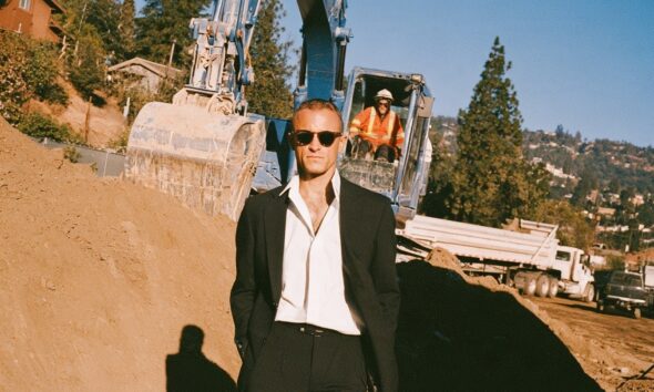 A male business owner standing in front of an excavator