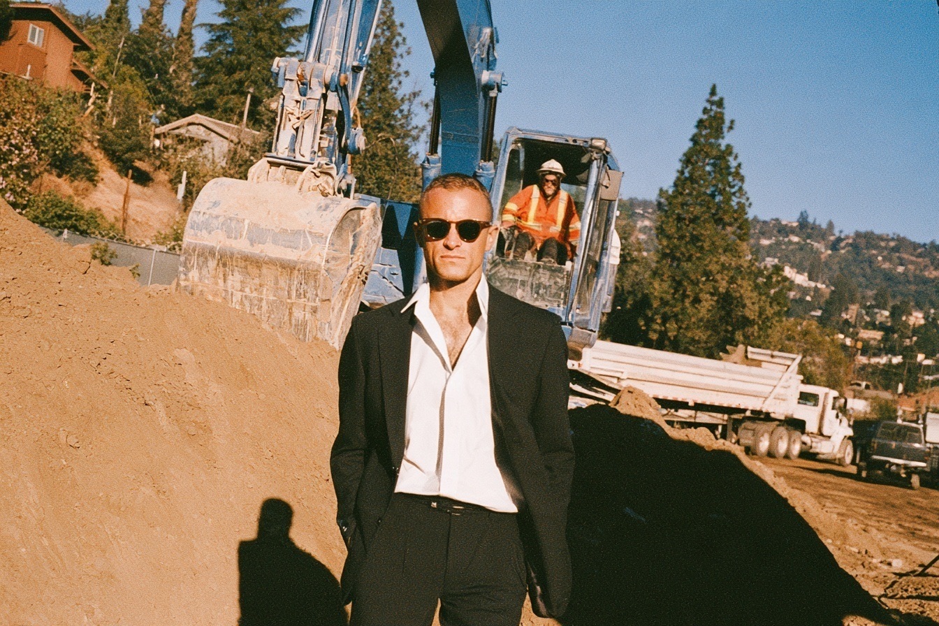 A male business owner standing in front of an excavator