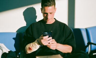 A male entrepreneur sitting in the sterile waiting room of an emergency clinic calmly reviewing documentation on a clipboard application while he has a bandaged forearm.