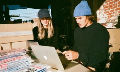 A man and woman entrepreneur looking at a laptop screen running an ecommerce store with products shipping out in the background