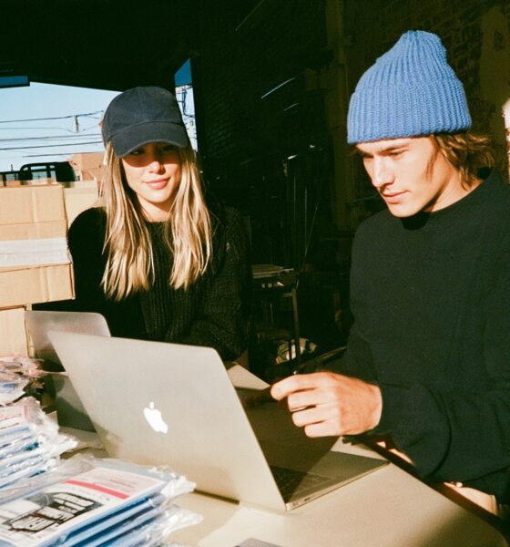A man and woman entrepreneur looking at a laptop screen running an ecommerce store with products shipping out in the background