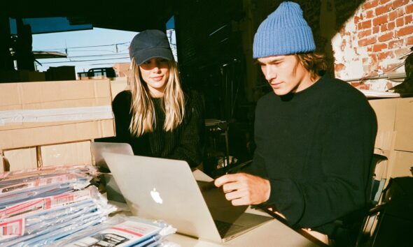 A man and woman entrepreneur looking at a laptop screen running an ecommerce store with products shipping out in the background