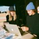 A man and woman entrepreneur looking at a laptop screen running an ecommerce store with products shipping out in the background