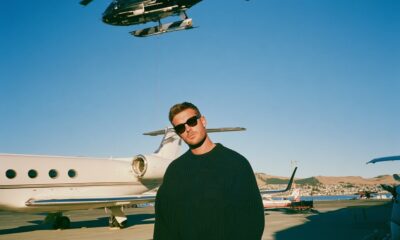 A man on the tarmac at the airport in a black sweater with helicopters and private planes around him in New Zealand