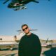A man on the tarmac at the airport in a black sweater with helicopters and private planes around him in New Zealand