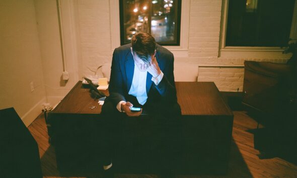 An entrepreneur founder staring at his phone in his office late at night feeling overwhelmed with tasks to do