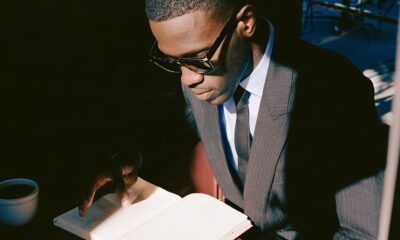 a black male founder in his mid-30s working early in the morning at a minimalist dark walnut desk to improve his life and ahcive more success