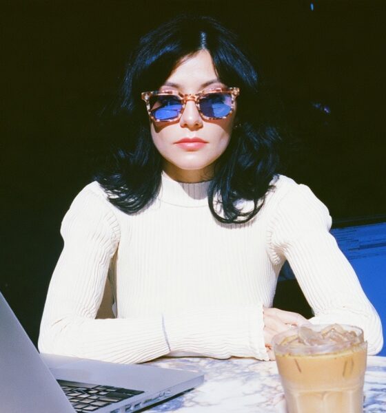 a female digital nomad wearing a white ribbed knit top and vintage tortoiseshell sunglasses sitting at an outdoor marble cafe table on her laptop working in Lisbon