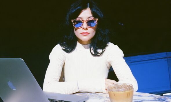 a female digital nomad wearing a white ribbed knit top and vintage tortoiseshell sunglasses sitting at an outdoor marble cafe table on her laptop working in Lisbon