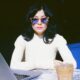 a female digital nomad wearing a white ribbed knit top and vintage tortoiseshell sunglasses sitting at an outdoor marble cafe table on her laptop working in Lisbon