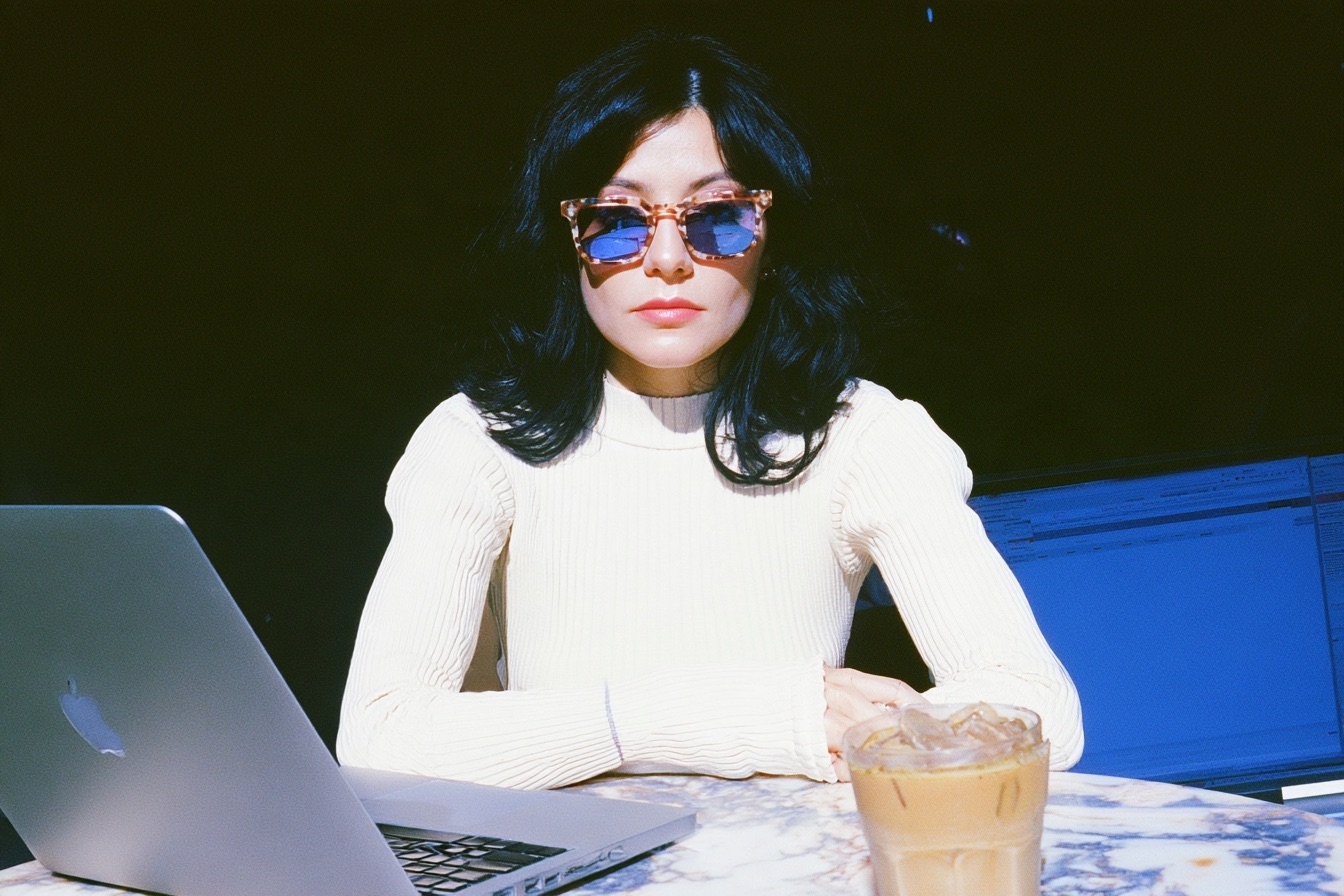 a female digital nomad wearing a white ribbed knit top and vintage tortoiseshell sunglasses sitting at an outdoor marble cafe table on her laptop working in Lisbon