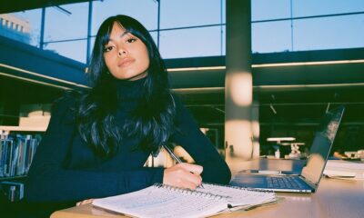 a focused young researcher sitting at a clean, sunlit wooden desk in an academic library