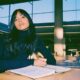 a focused young researcher sitting at a clean, sunlit wooden desk in an academic library
