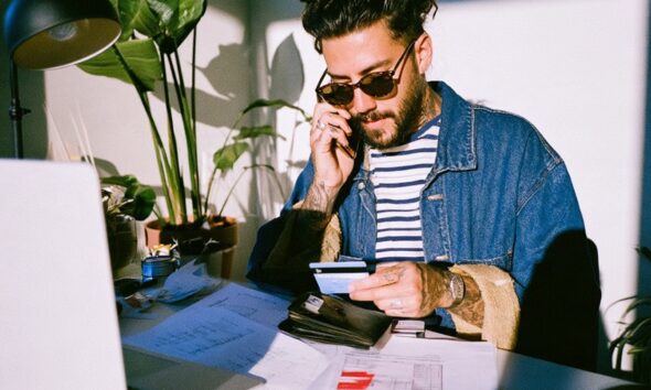 a male entrepreneur with his wallet out in his neat modern home office space applying for a loan