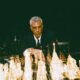 a sharply dressed male entrepreneur in his early forties sitting alone across an enormous luxury black marble chessboard inside a dark executive penthouse