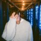 a stressed male tech founder in a grey heavy knit sweater standing inside a massive dimly lit server farm