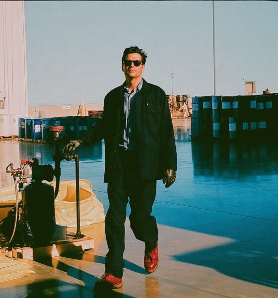 a successful plant manager in a tailored work jacket walking a fluid transfer line with his gloved hand resting near a pump and check valve assembly in his business warehouse