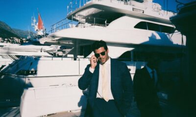 male entrepreneur in a navy linen suit standing confidently on the teak deck of a massive superyacht moored in a luxury marina in Montenegro