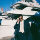 male entrepreneur in a navy linen suit standing confidently on the teak deck of a massive superyacht moored in a luxury marina in Montenegro