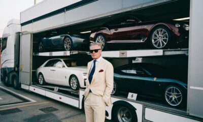 a man standing by a luxury car carrier truck with luxury cars in the carrier of the truck