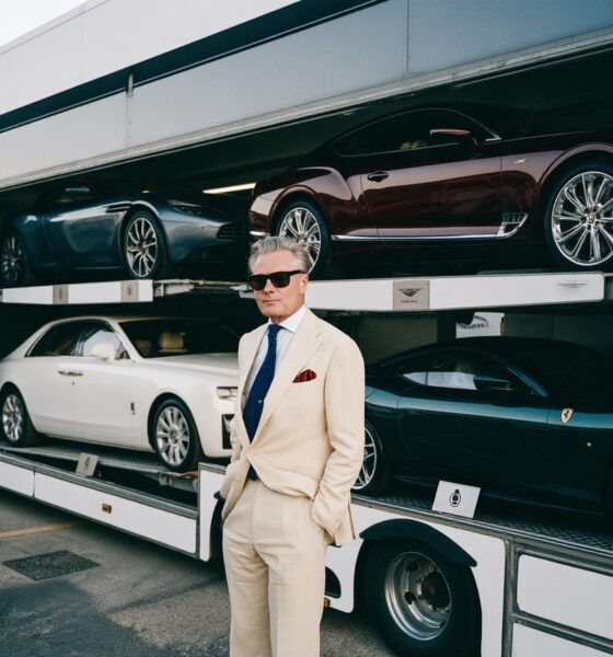 a man standing by a luxury car carrier truck with luxury cars in the carrier of the truck