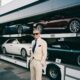 a man standing by a luxury car carrier truck with luxury cars in the carrier of the truck