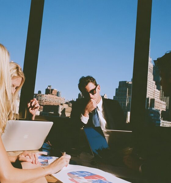 three executives from sales, marketing and finance sitting in a sleek glass walled boardroom.