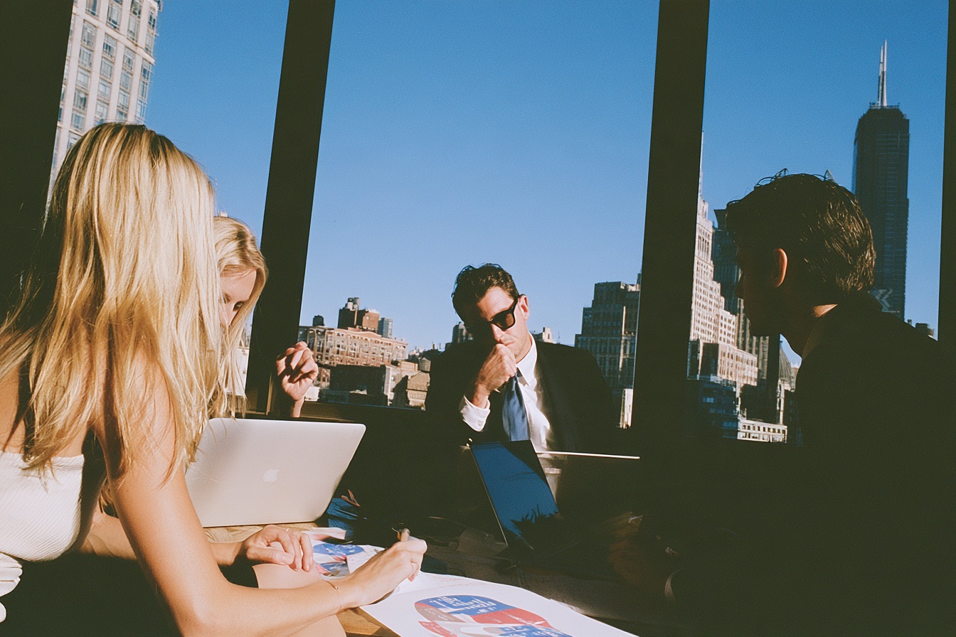 three executives from sales, marketing and finance sitting in a sleek glass walled boardroom.